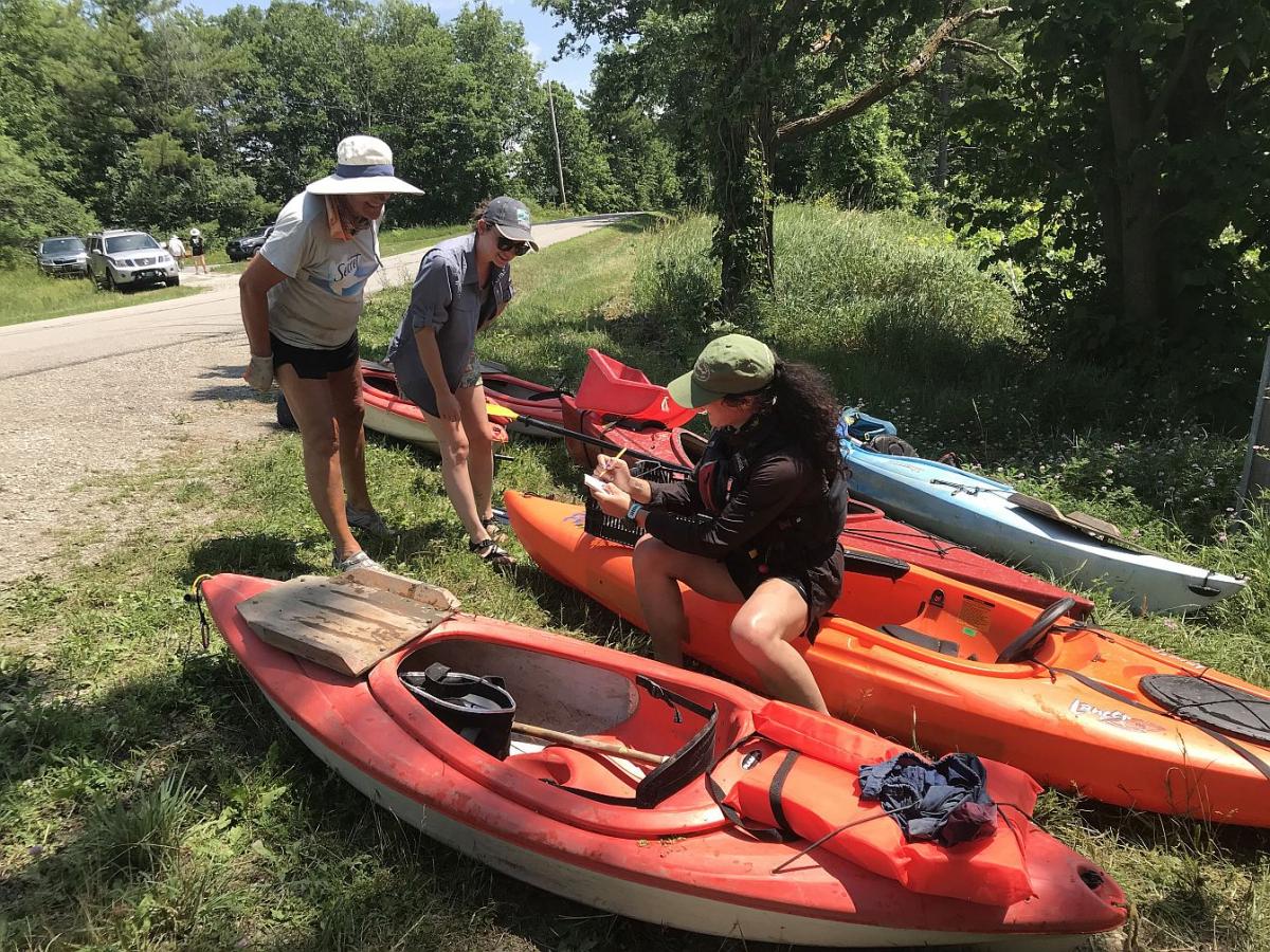 Women and Kayaks are seen in a grassy area along the side of a road