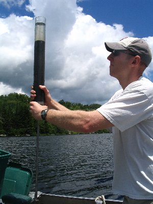 Man collecting water samples from a lake, using a tall tube