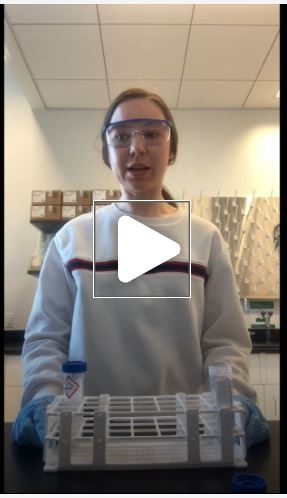 "A screenshot of a video on Total Nitrogen Sample Acification.  A person is seen wearing safety goggles and gloves holding a tray with test tubes in it."
