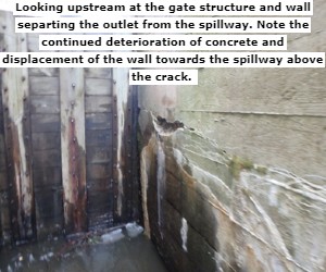 Looking upstream at the gate structure and wall separting the outlet from the spillway. Note the continued deterioration of concrete and displacement of the wall towards the spillway above the crack. 