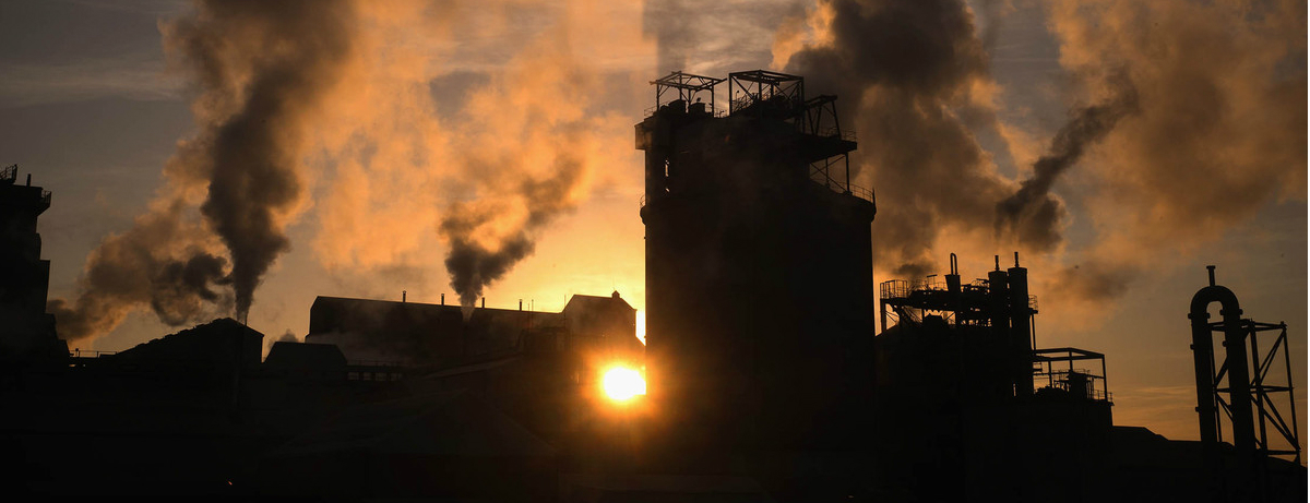 Smoke stacks with sunset between buildings