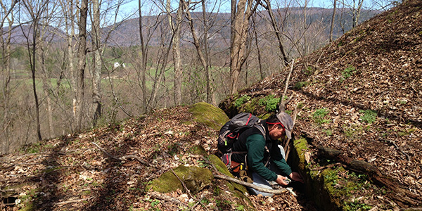 Man exploring leaf-littered fractured rock in late autumn