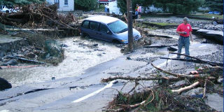 Road filled with tree branches, road washout, flooded vehicle