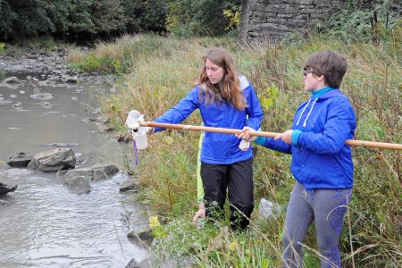 Image of 2 students using a river dipper to collect a water sample from a river