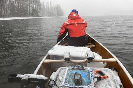 Image of an Ecologist paddling a canoe full of water quality monitoring equipment on a lake during early spring