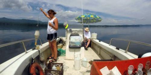 Boat with monitoring tools out on the lake, woman taking water samples from the boat