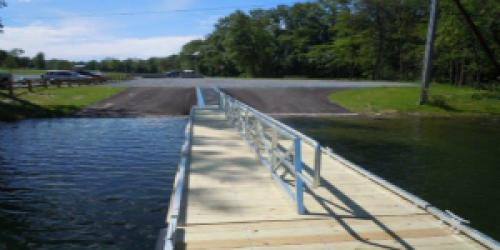 a long wooden boat dock with hand rail stretches out over the lake on a sunny day