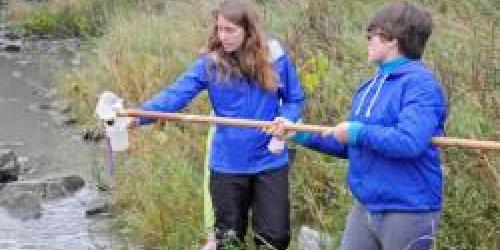 two people collecting a water quality sample by a river