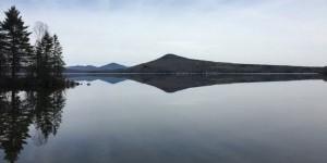 Calm lake with conifer trees on left and mountain in background
