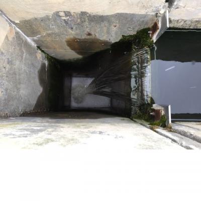 A photo of a water flowing through a narrow concrete passage and falling into a concrete pit