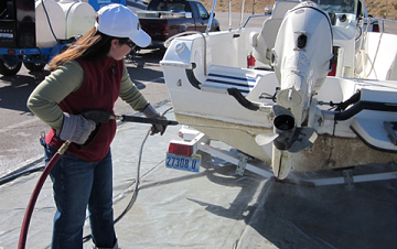 A woman sprays a boat's propeller with a high pressure jet of water.