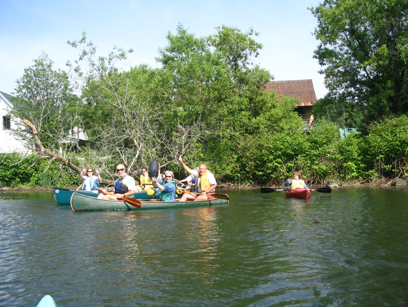 six people seen in two green canoes on the right, one closer to the foreground.  Another person seen in a red kayak at the left.