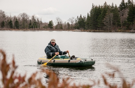 man performing Cold weather sampling at remote Little Pond in an inflatable raft