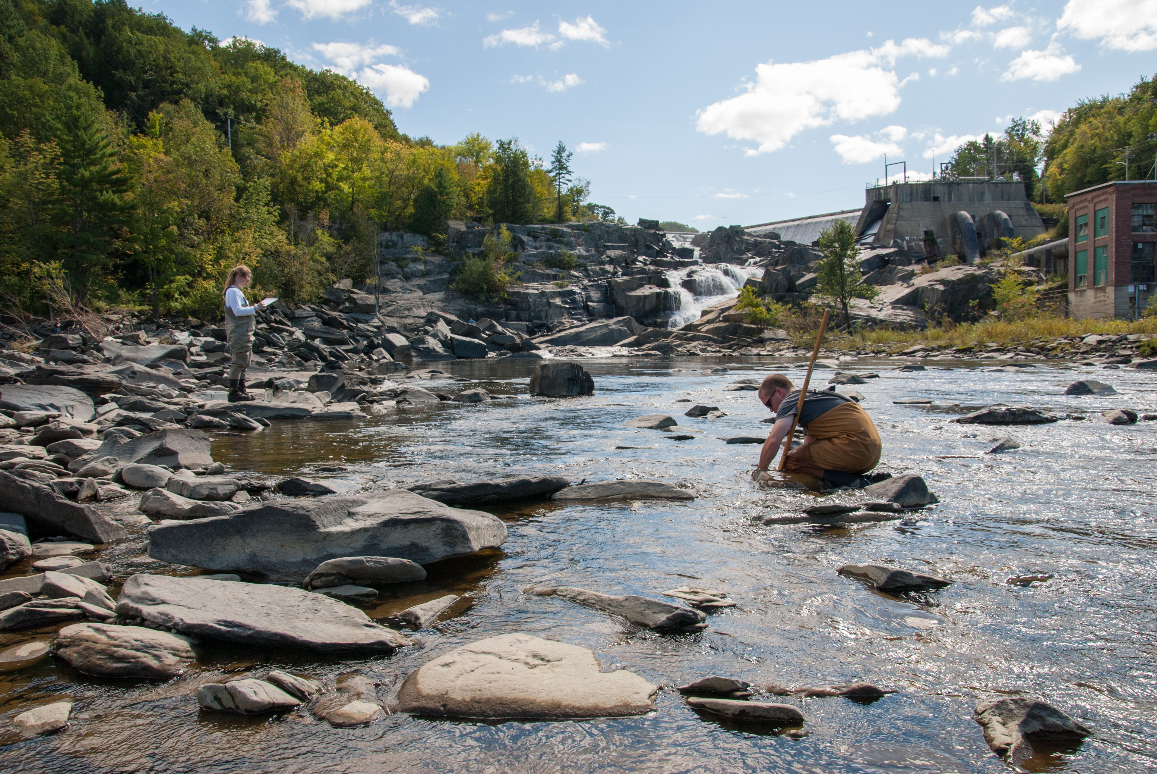 A rocky stream with two people taking water samples.