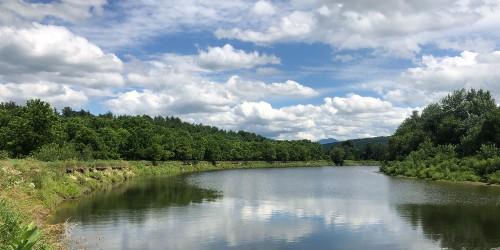 River with green banks and reflecting blue sky with clouds