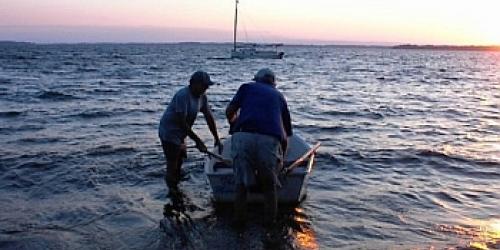 Two people standing with a rowboat in the shallow water of Lake Champlain at sunset.